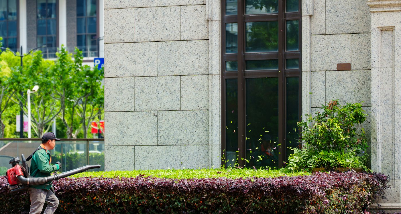 Landscaper trimming hedges beside a commercial building